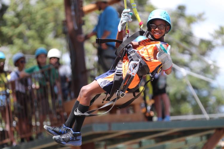 A photo of a boy strapped in securely for Ziplining with Action Zipline Tours, he is wearing thick gloves and a helmet.