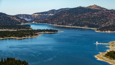 An aerial view of Big Bear Lake. It is a sunny day, with clear blue skies and green pine forests surround the blue lake.