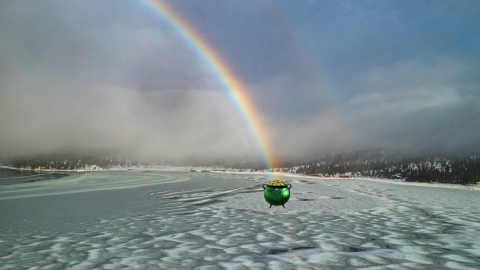 A picture of a Saint Patrick's Day pot of gold found at the end of a rainbow in the midst of a snow covered lakeside.