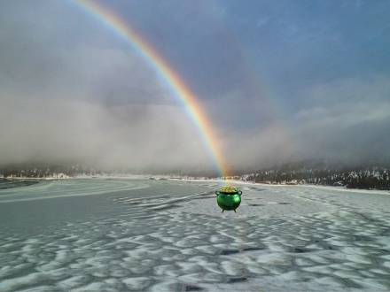 A picture of a Saint Patrick's Day pot of gold found at the end of a rainbow in the midst of a snow covered lakeside.