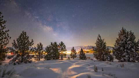 A photo of Big Bear's night sky taken during winter after a snowfall, the bright stars and a galaxy are visible.