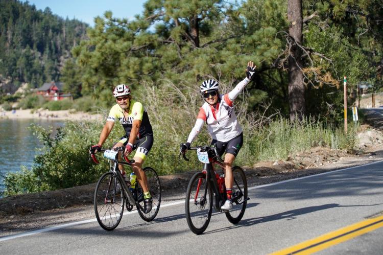 Two cyclists wave during their Tour de Big Bear bike ride in Big Bear Lake, CA