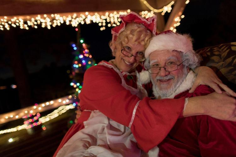 A photo of Mrs and Mr Claus sitting together during at the Christmas Farms, the background sporting lovely Christmas lights.