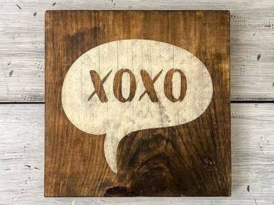 A wooden sign painted with XOXO sits on a white background.