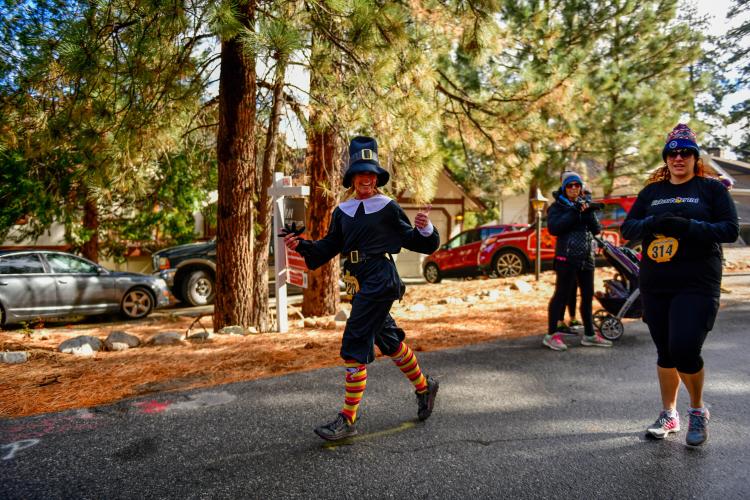 Two female racers participating in the autumn Thanksgiving Turkey Trot, one lady is wearing a black colored pilgrim costume.