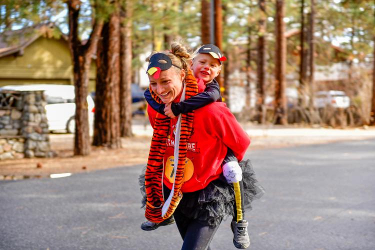 A photo of a mother with a turkey mask racing while carrying her child on her back during the Thanksgiving Turkey Trot event