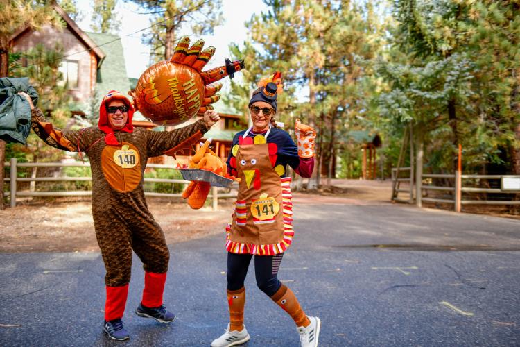 A photo of a couple in their turkey costumes during the Thanksgiving Turkey Trot, the lady is holding a fake roast turkey.