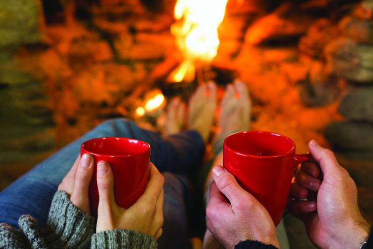 a couple holds cups of hot cocoa by the fire in Big Bear